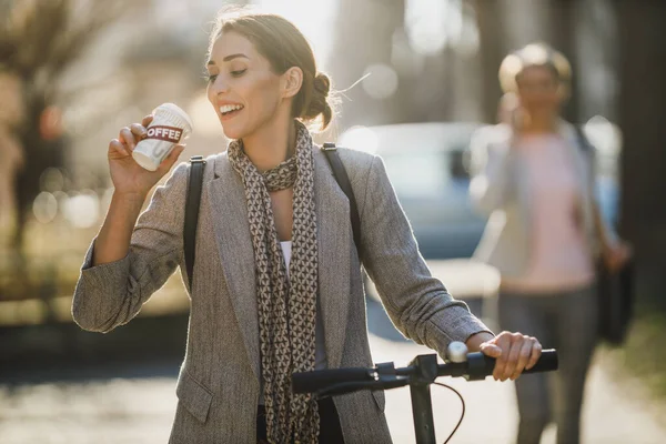 A young businesswoman drinking coffee during go to work with an electric push scooter.