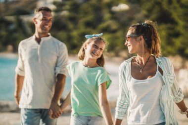 Gülümseyen bir genç kız ve ailesi yaz tatilinde eğlenirken deniz kenarında yürüyorlar..