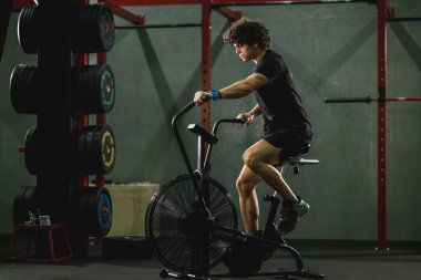 Genç kaslı bir adam spor salonunda motorlu taşıt eğitimi alıyor..