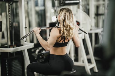 Genç, kaslı bir kadın spor salonunda makineyle antrenman yapıyor..