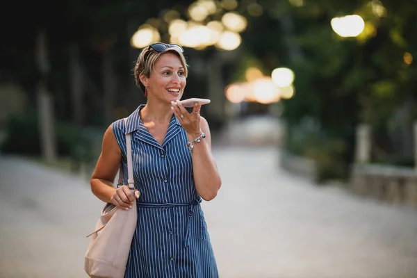Mulher Atraente Madura Usando Smartphone Andando Noite Enquanto Desfruta Umas — Fotografia de Stock