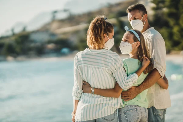保護N95マスクを持つ幸せな受け入れ家族の背面ビューコロナパンデミックでビーチでの時間を過ごす — ストック写真