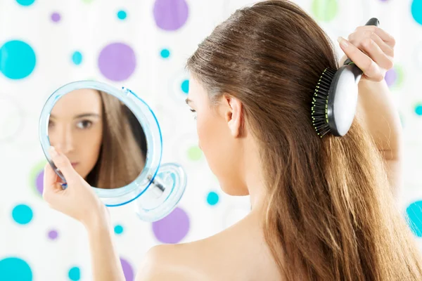 Chica con un espejo peinándose el pelo — Foto de Stock