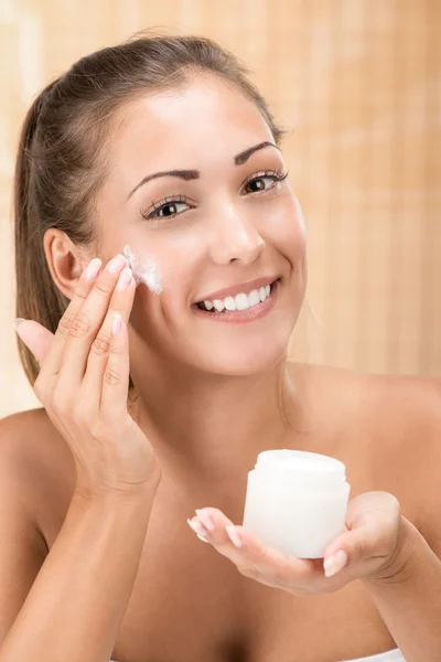 Mujer joven poniendo crema facial —  Fotos de Stock