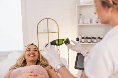 Kadın güzellik uzmanı, koruyucu gözlük tutarken müşteriyi lazer epilasyonuna hazırlıyor. 