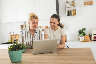 Anne ve kızı modern bir mutfakta dizüstü bilgisayarda birlikte çalışıyorlar., 