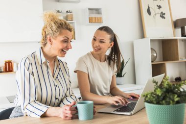Anne ve kızı modern bir mutfakta dizüstü bilgisayarda birlikte çalışıyorlar., 