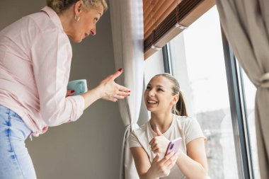Anne ve kızı güneşli bir günde pencerenin önünde neşeli ve sıradan bir sohbet ederler.. 