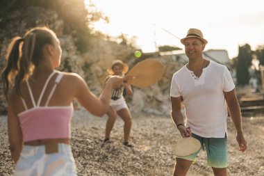 Anne onların fotoğraflarını çekerken baba ve kızı plajda raketbol oynuyorlar.. 