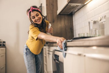 Kadın mutfak tezgahını bez ve sprey şişeyle silip dezenfekte ediyor..