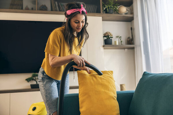 Женщина проводит глубокую уборку и пылесосит диван на весенней уборке дома. 