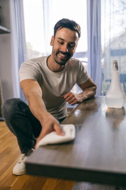 Gülümseyen adam evini korumak için rutin işleri yaparken masa yüzeyini temizliyor.. 