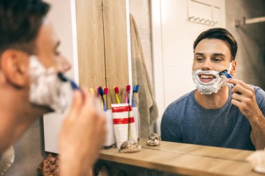 Genç bir adam tıraş olurken tıraş olurken jiletle sabahları banyoda. 