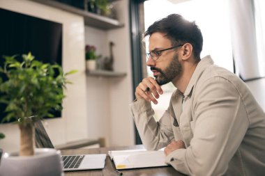 Gözlüklü genç adam ev ofisinde dizüstü bilgisayarla çalışıyor.. 