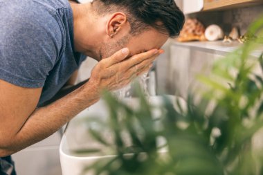 Adam evdeki tuvalette sabah rutinini yaparken lavaboda yüzünü temizliyor.. 