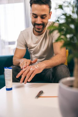 Gülümseyen adam evde otururken eline losyon sürüyor.. 