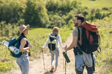 Sırt çantalarıyla dağlarda yürüyüş yapan ve güneşli bir günde sırıkla yürüyüş yapan arkadaşların arka görüntüsü.. 