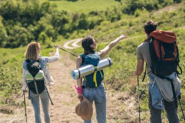 Güneşli bir günde sırt çantaları ve yürüyüş direkleriyle yürüyüş yapan üç mutlu arkadaş.. 