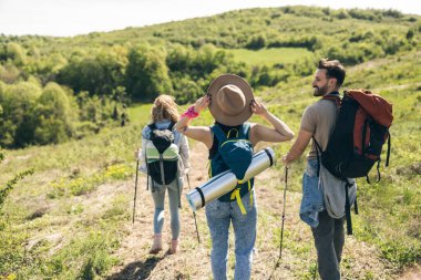 Güneşli bir günde sırt çantaları ve yürüyüş direkleriyle yürüyüş yapan üç mutlu arkadaş.. 
