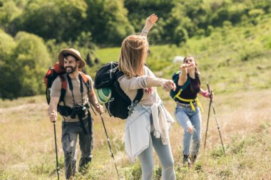 Neşeli üç arkadaş, güneşli bir günde sırt çantaları ve yürüyüş direkleriyle yürüyüş gününün tadını çıkarıyorlar.. 