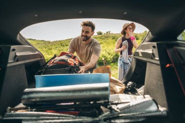 Mutlu ve gülümseyen genç arkadaşlar doğada arabadaki eşyalarla eğlenmeye hazırlanıyorlar.. 