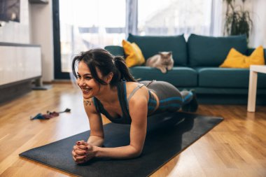 Genç kadın evde yoga minderinde karın kası egzersizi yapıyor..