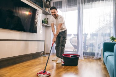 Evde yerleri silip süpüren gülümseyen genç adam..