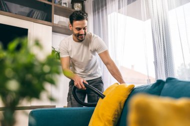 Genç adam oturma odasında kanepesini temizliyor ve süpürüyor..