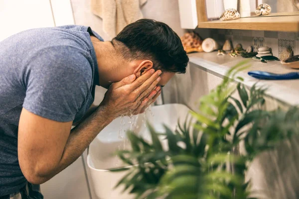 Adam evdeki tuvalette sabah rutinini yaparken lavaboda yüzünü temizliyor..