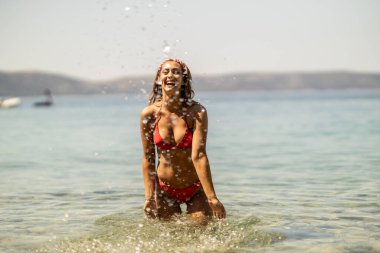 Bikinili çekici genç bir kadın yaz günü sahilde oturuyor ve eğleniyor..