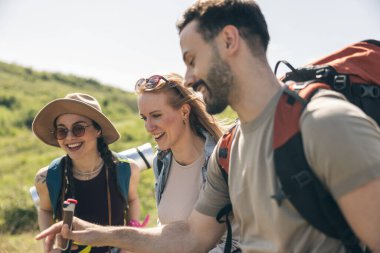 Üç arkadaş güzel bir bahar gününde sırt çantaları ve yürüyüş direkleriyle yürüyüş yapıyor..