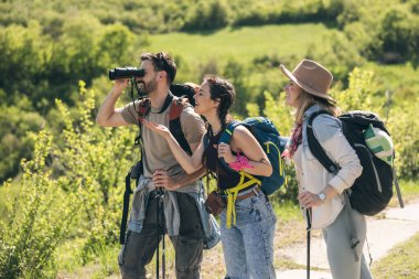 Mutlu arkadaşlar güneşli bir günde yürüyüş yaparken dürbünle kırları keşfediyorlar..