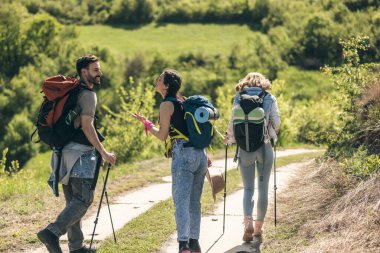 Güneşli bir günde sırt çantaları ve yürüyüş direkleriyle yürüyüş yapan üç mutlu arkadaş..