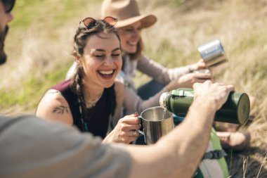 Güneşli bir günde kırsalda yürüyüş yapan arkadaşlar piknik yapıyor..