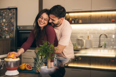 Mutlu ve gülümseyen çift mutfakta blender ile taze meyve suyu yapıyor..