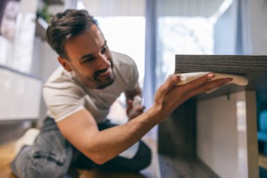 Genç adam evdeki tozu bez ve spreyle temizliyor..