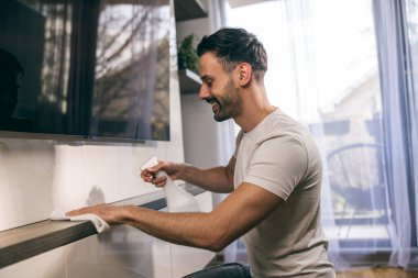 Oturma odasındaki tozları silerken günlük ev işlerini yapan bir adamın fotoğrafı..