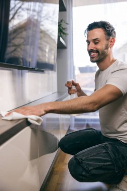 Oturma odasındaki tozları silerken günlük ev işlerini yapan bir adamın fotoğrafı..
