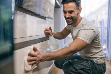Oturma odasındaki tozları silerken günlük ev işlerini yapan bir adamın fotoğrafı..