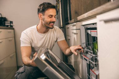 Bulaşıkları yıkayan ve bulaşık makinesinden bulaşıkları çıkaran bir adam..