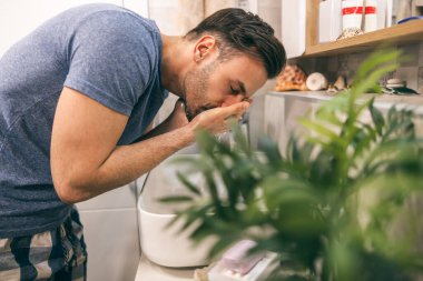 Adam evdeki tuvalette sabah rutinini yaparken lavaboda yüzünü temizliyor..