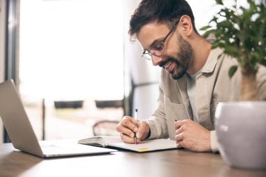 Gözlüklü genç adam ev ofisinde dizüstü bilgisayarla çalışıyor..