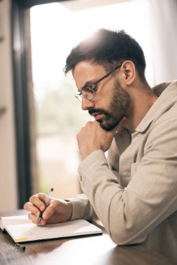 Gözlüklü genç adam evde otururken ve yazarken dizüstü bilgisayarda çalışıyor..
