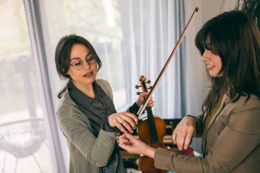 Müzik eğitmeninin öğrenciyle özel keman dersi var ve ona keman tutmayı öğretiyor..