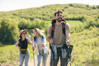 Üç neşeli arkadaş kırsalda yürürken ve yürürken güneşli bir günün tadını çıkarıyorlar..