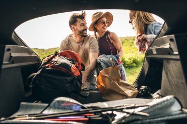 Mutlu ve gülümseyen genç arkadaşlar doğada arabadaki eşyalarla eğlenmeye hazırlanıyorlar..