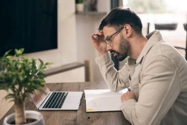 Gözlüklü genç adam evde otururken ve yazarken dizüstü bilgisayarda çalışıyor..