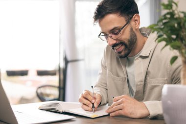 Gözlüklü genç adam ev ofisinde dizüstü bilgisayarla çalışıyor..