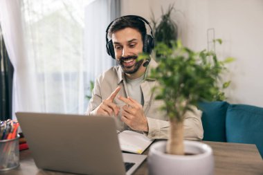 Kulaklıklı genç adam evdeki bilgisayarında video görüşmesi yapıyor..