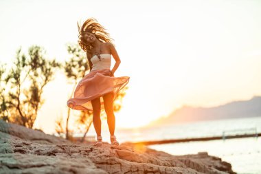 An attractive young woman in dress is enjoying summer sunset at the wonderful seaside.